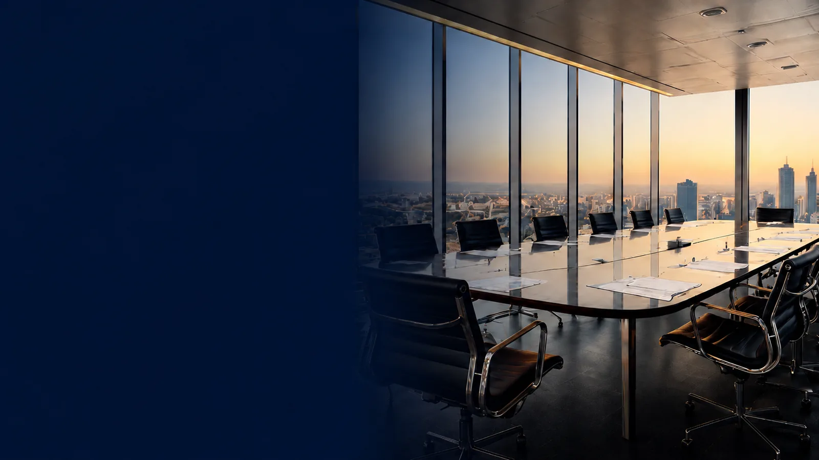 A boardroom table beside floor-to-ceiling windows overlooking a city skyline at sunset.