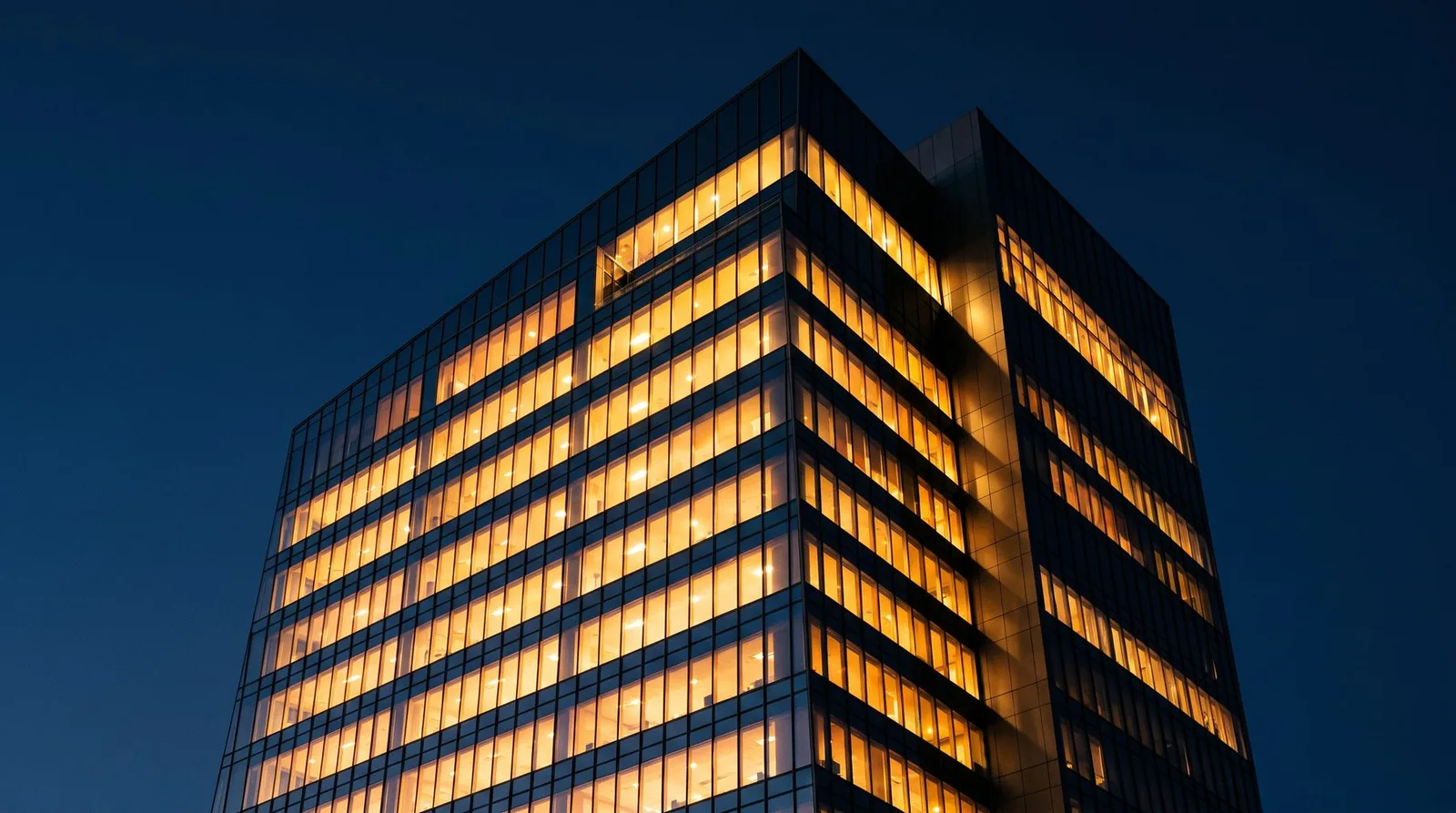 A lit office tower at dusk, seen from below.